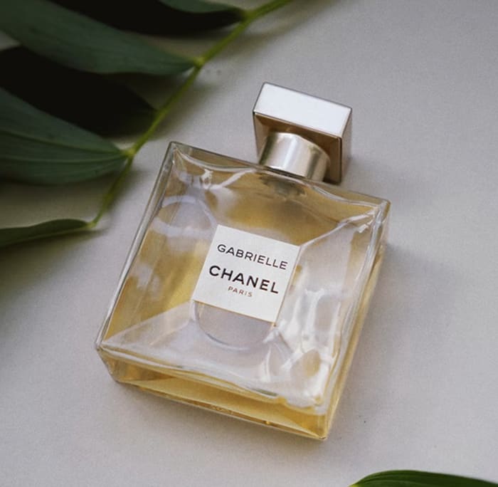 A square bottle of Gabrielle Chanel perfume with gold liquid on a neutral background